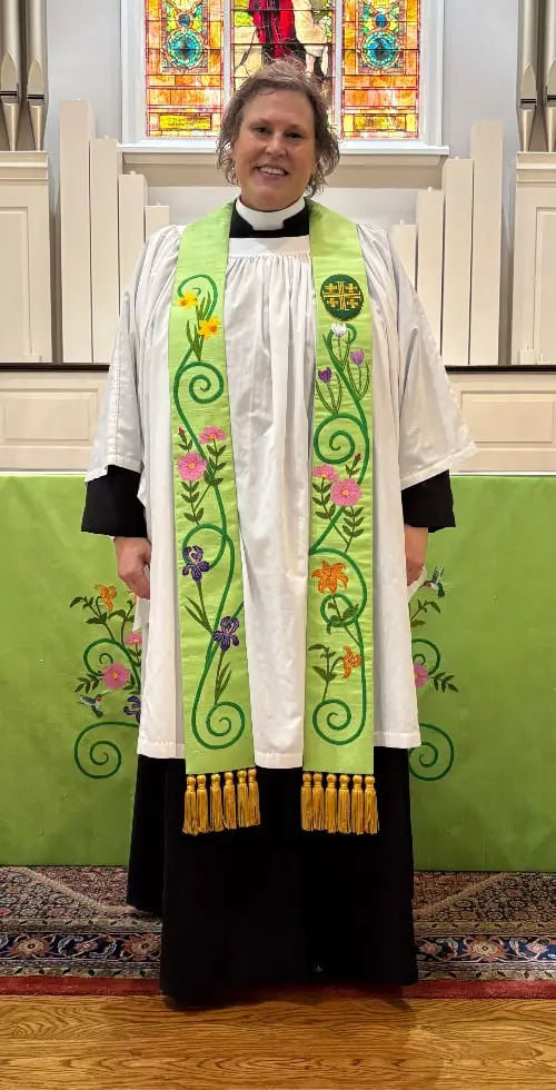 A Priest modeling her custom stole that coordinates with the altar cloth in the background. Both are a bright green color with florals.